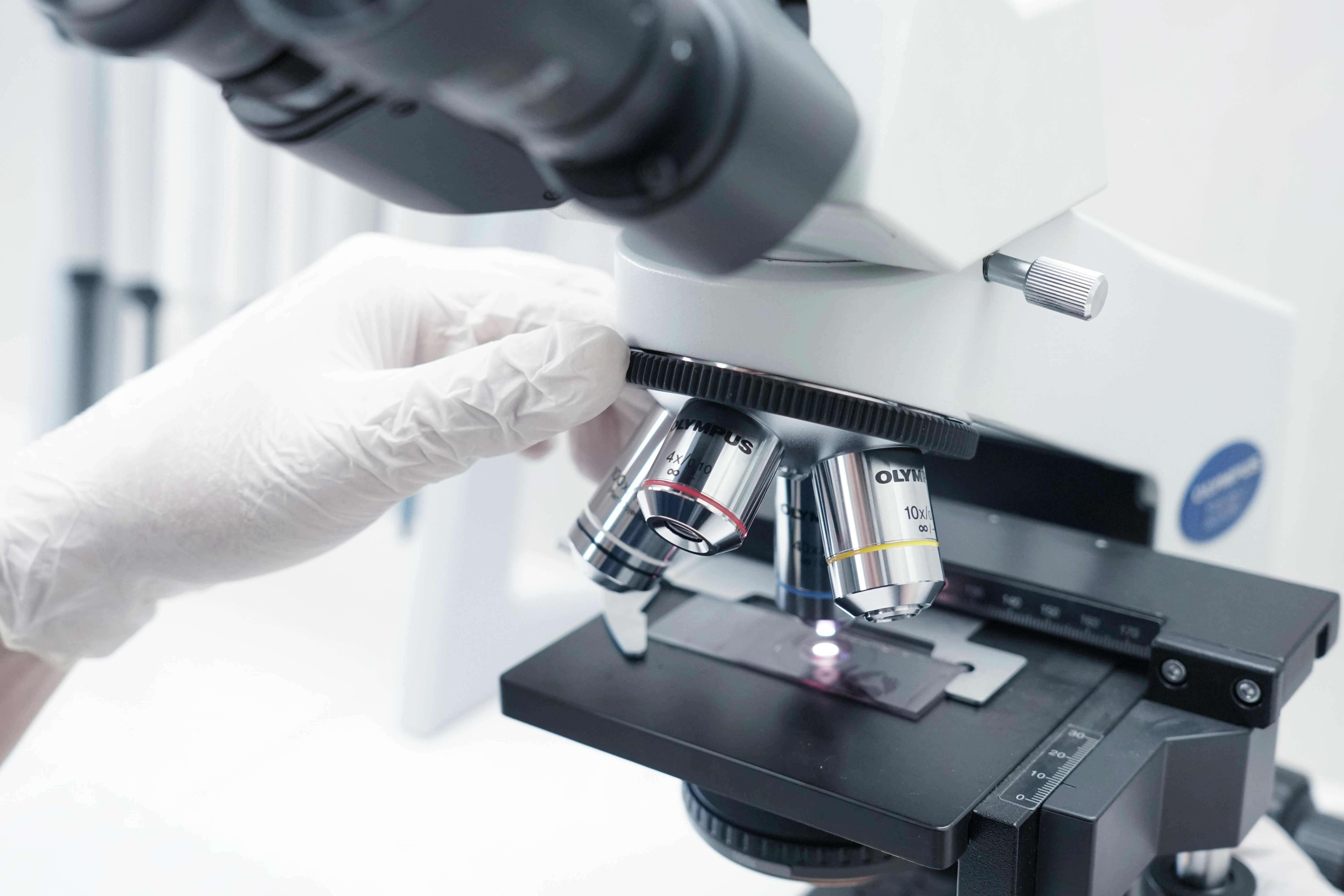 Gloved hand adjusting a slide on a lab microscope